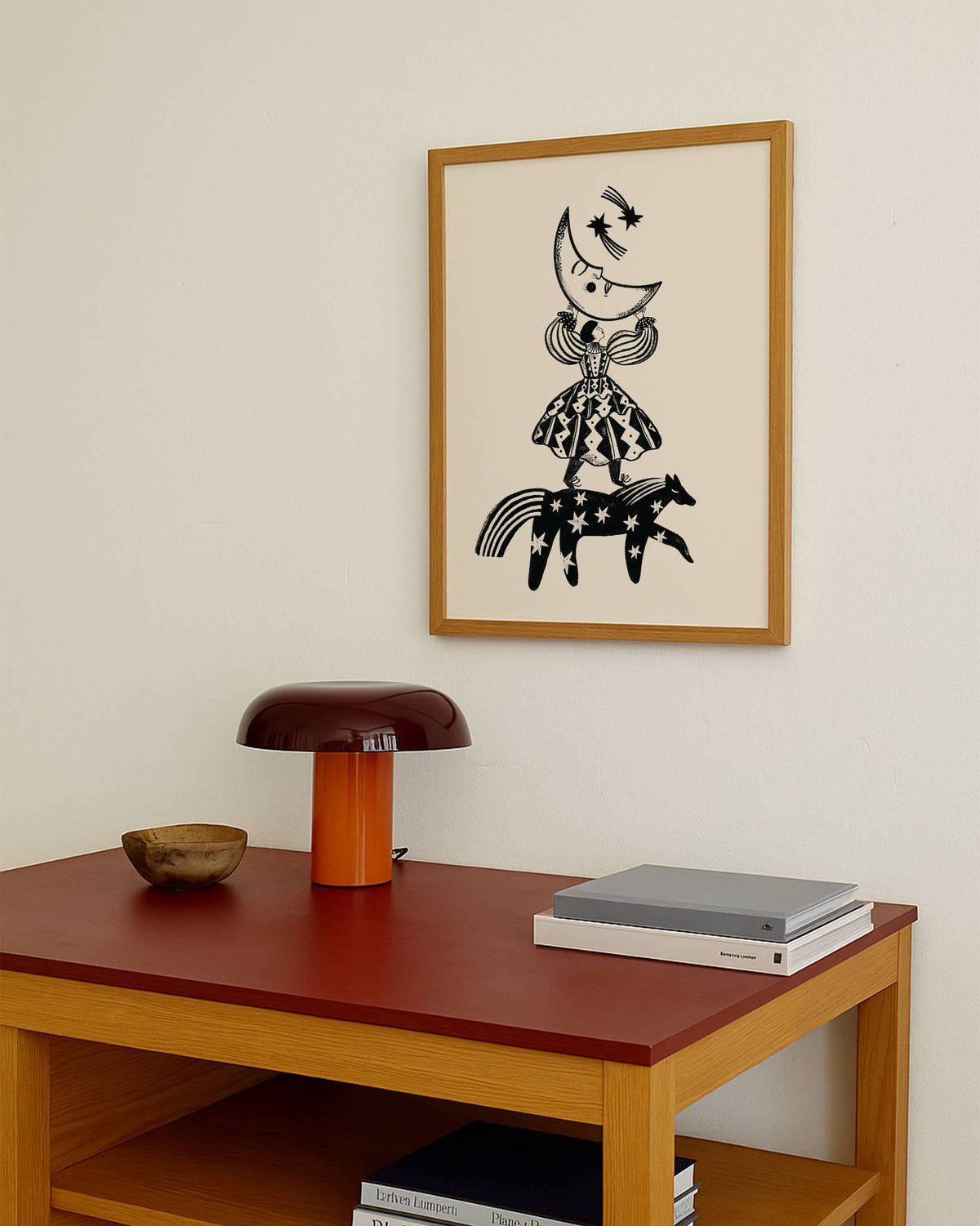 Ingelijste illustratie Folkdromer van Carole Hillman aan de muur boven een houten tafel met een oranje vintage tafellamp