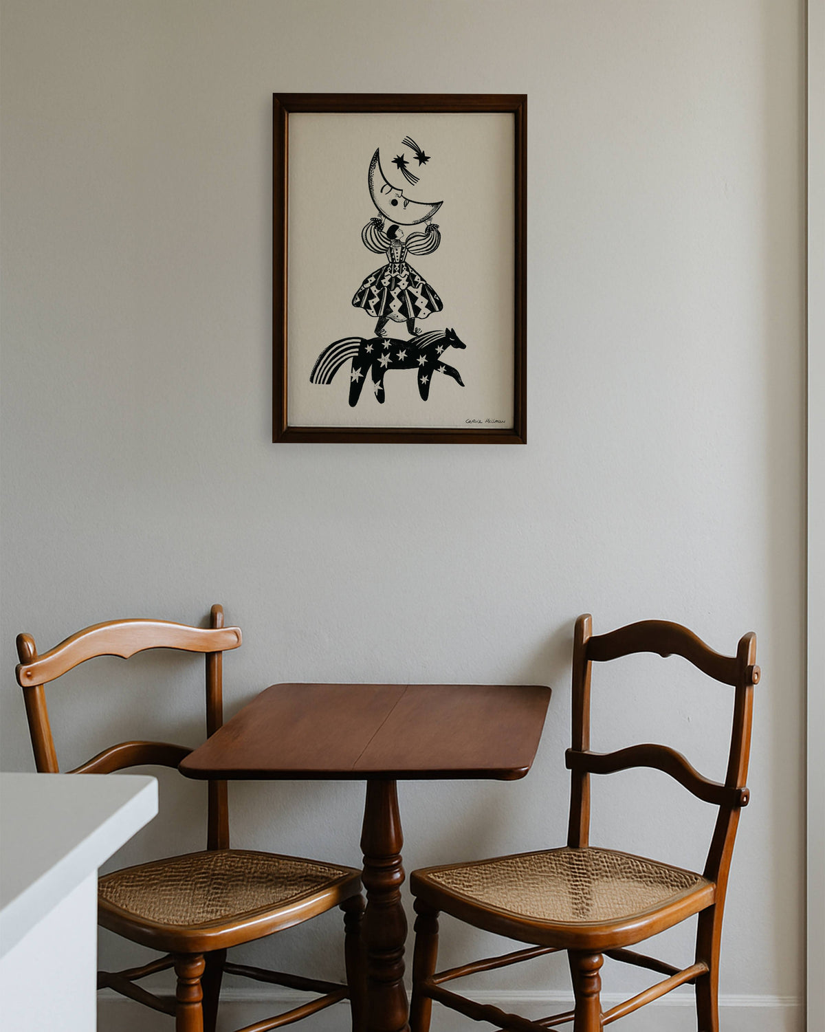 Ingelijste poster Folkdromer van Carole Hillman in donkerhouten lijst boven een vintage bistro tafeltje met houten stoelen