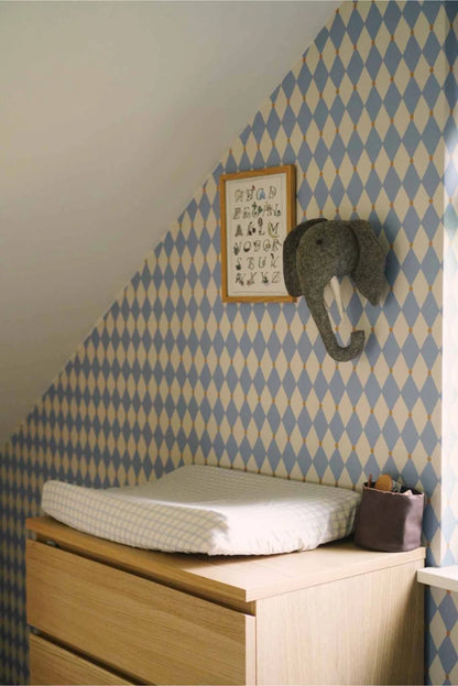 Schuine wand in de kinderkamer bekleed met lichtblauw harlekijn behang en een olifantenkop wanddecoratie