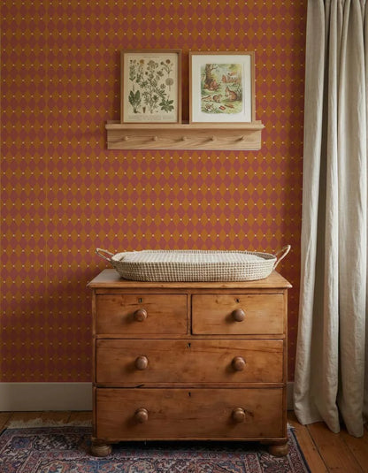 Stijlvolle babykamer met een houten commode en een warme accentmuur van Atelier Chien harlekijn behang in rood oranje