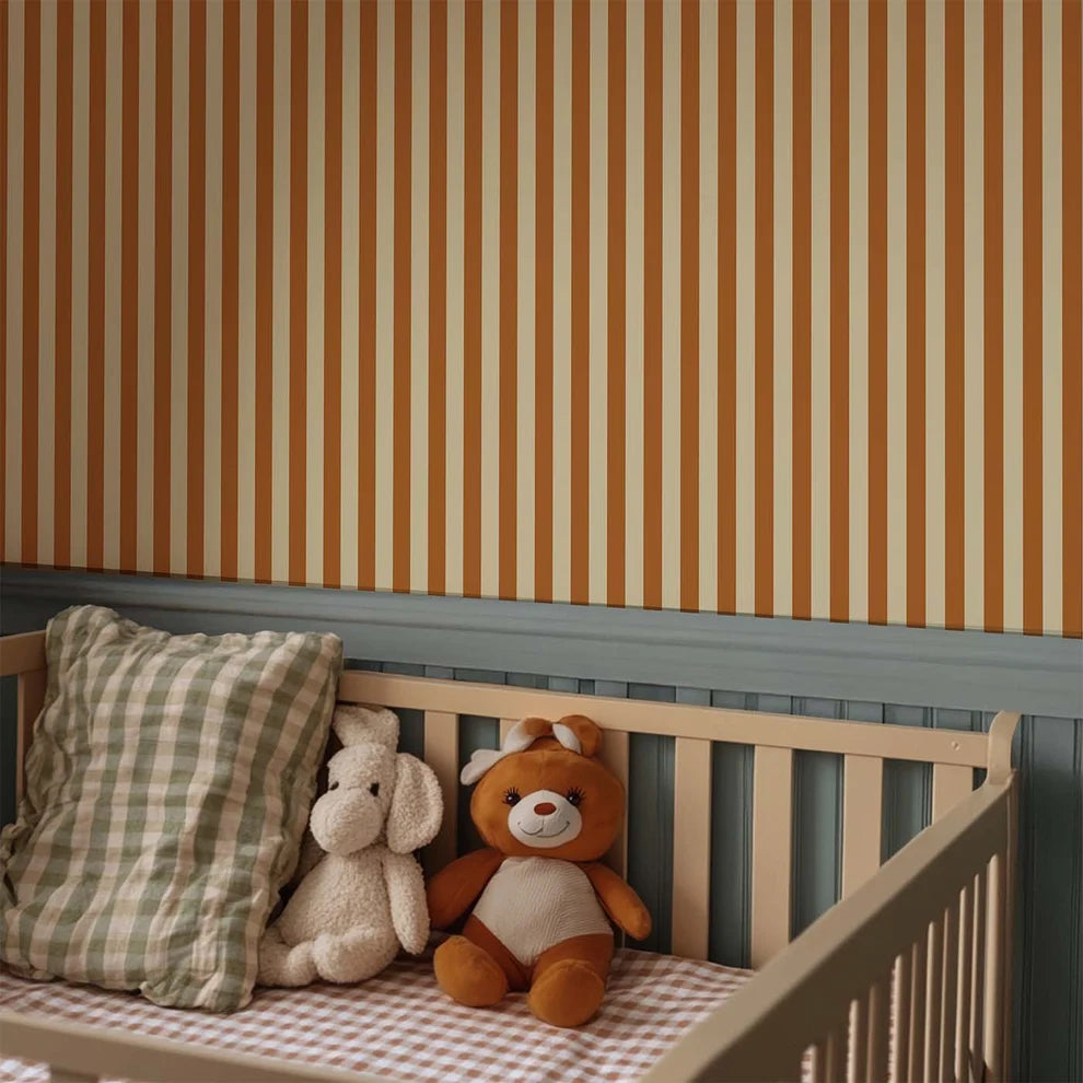 Atelier Chien mat vliesbehang met smalle oranje strepen boven een kinderbedje met knuffels