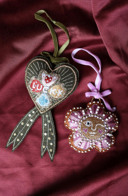 All The Luck In The World olijfgroen Lucky Clover Bow hart-ornament naast een roze zon-ornament
