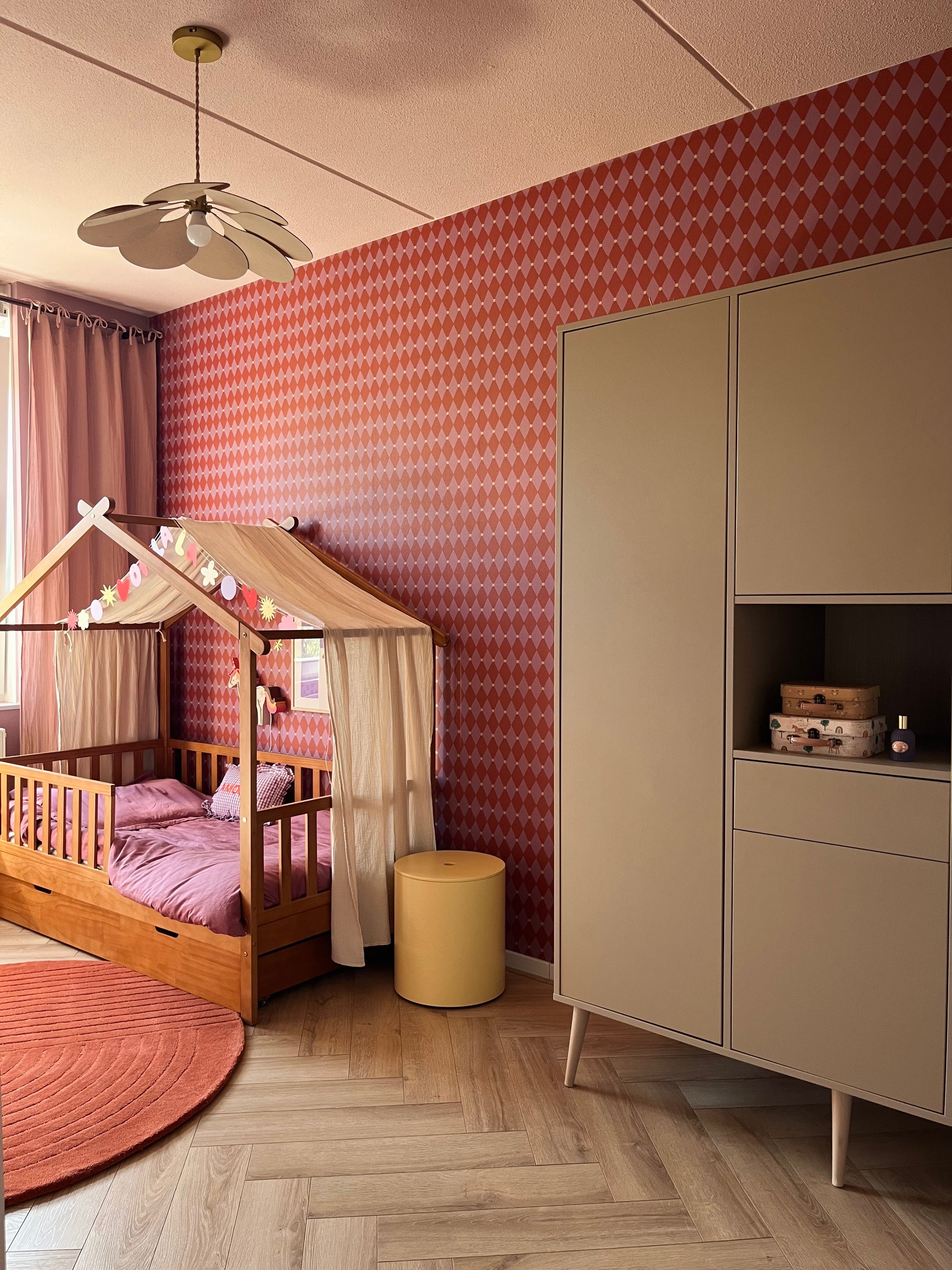 Kinderkamer gestyled met roze en rood harlekijn behang van Atelier Chien op de muur.