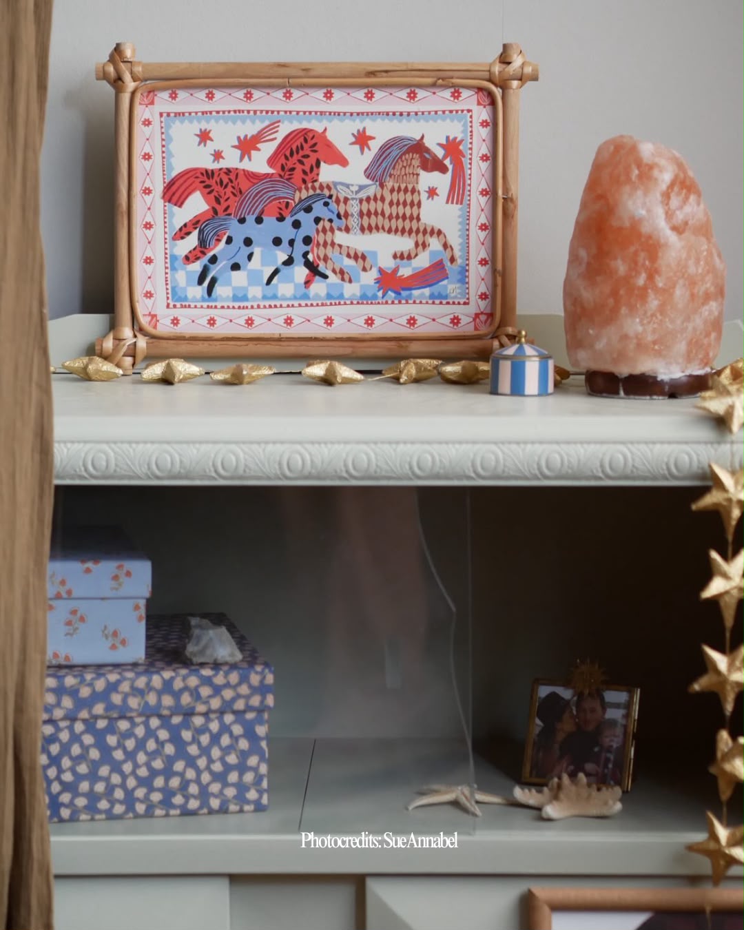 Kleurrijke Carole Hillman kunstposter in bamboe lijst op een kast met een zoutlamp en sterrendecoratie in een kinderkamer
